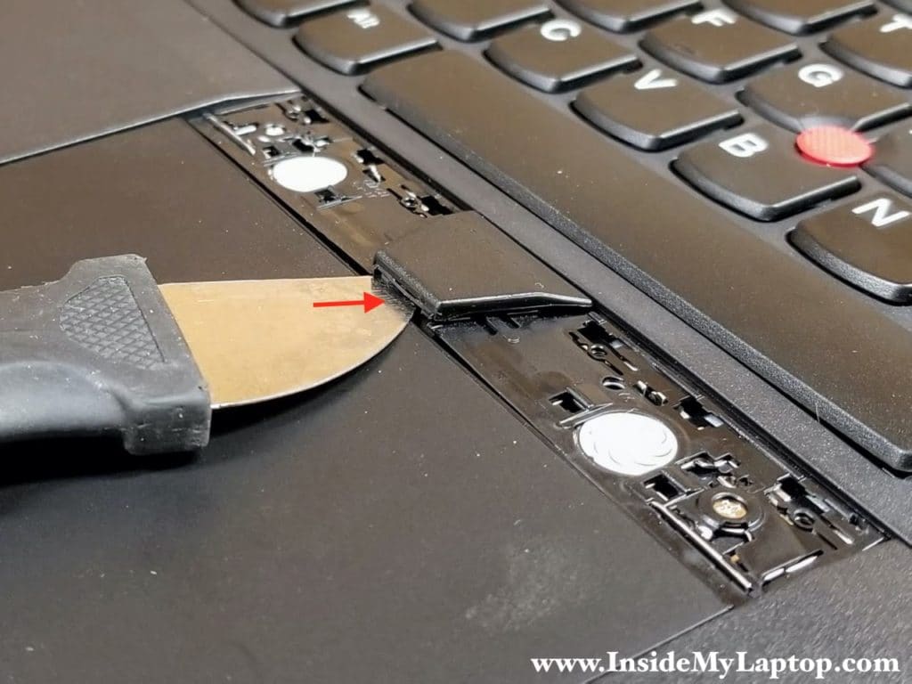 Insert the case opener tool under the middle button to elevate the keyboard frame above two T-shaped knobs.